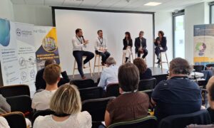 Table ronde dans une salle du CEA Tech. Les 4 intervenants et l'animatrice sur une estrade devant du public
